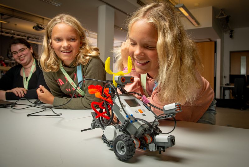 Girls are testing a little robot and they smile.