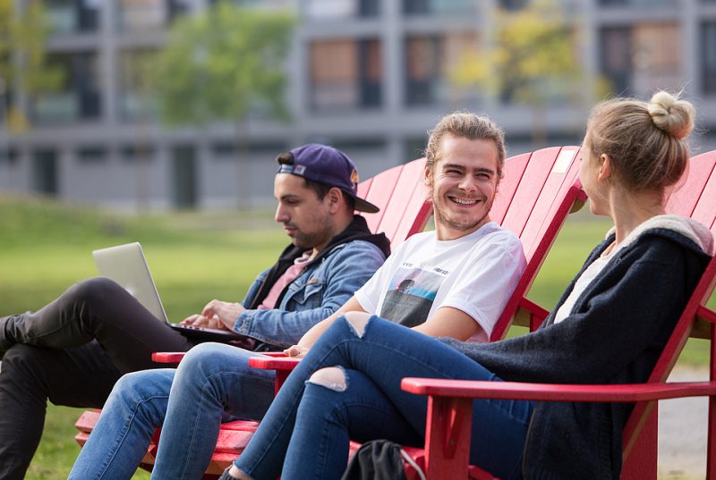 Three people sitting on chairs and smile outside